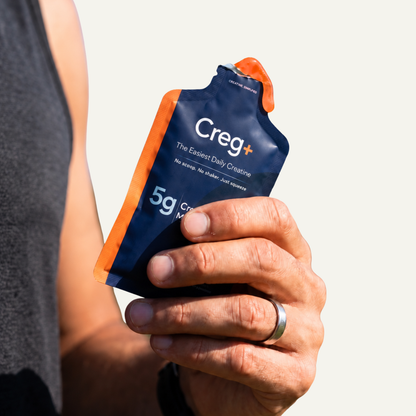 Close-up of a hand holding an opened navy and orange CREG+ creatine gel sachet.